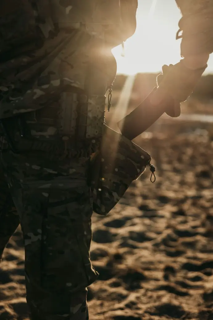 A soldier holds a weapon in sunlight.